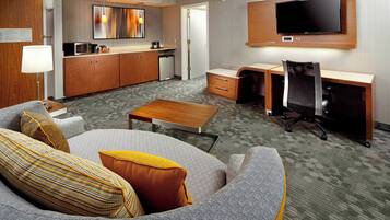 A hotel room with a sofa, a desk, a television, a microwave, and a small kitchenette.