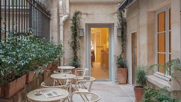 A courtyard with outdoor seating, potted plants, and a building entrance. - Hôtel Basss (Paris)