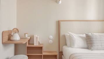 Un dormitorio con cabecera de madera, una mesita de noche con tetera, libros y una lámpara.