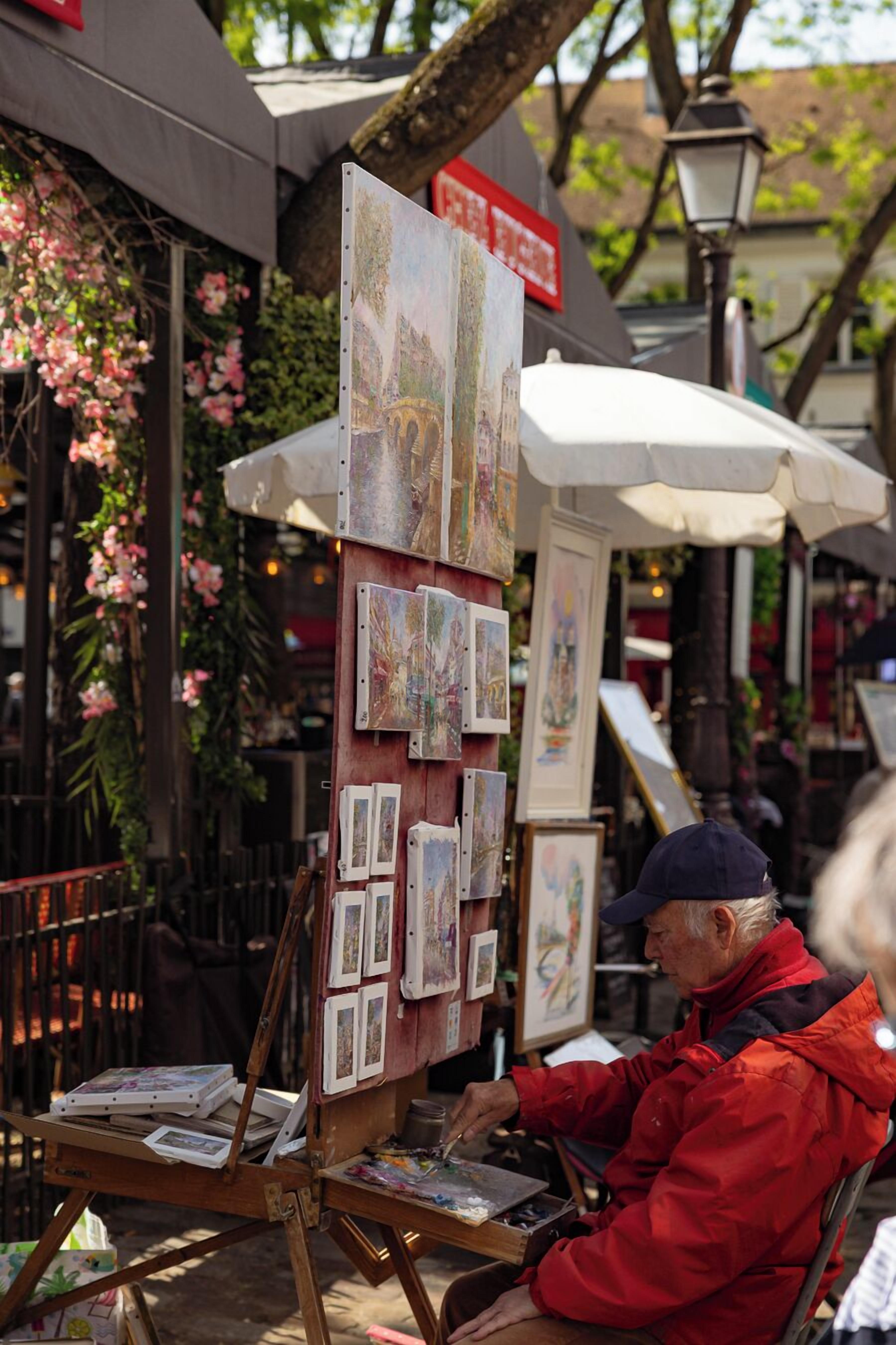 An outdoor art display with paintings on easels and a person painting.