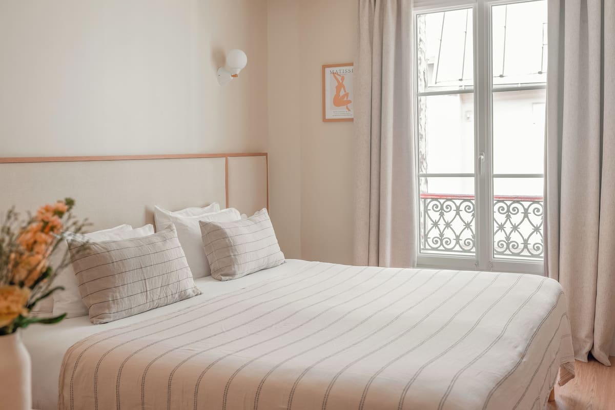 Un lit bien fait, avec une literie à rayures, un luminaire fixé au mur et une fenêtre avec des rideaux.