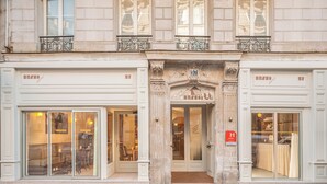 Un hotel con fachada clásica, amplios ventanales y una entrada destacada con un arco decorativo.