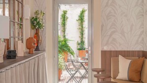 A room with a sofa, a table, a chair, a bar area, and a door leading to an outdoor patio with plants. - Hôtel Basss (Paris)