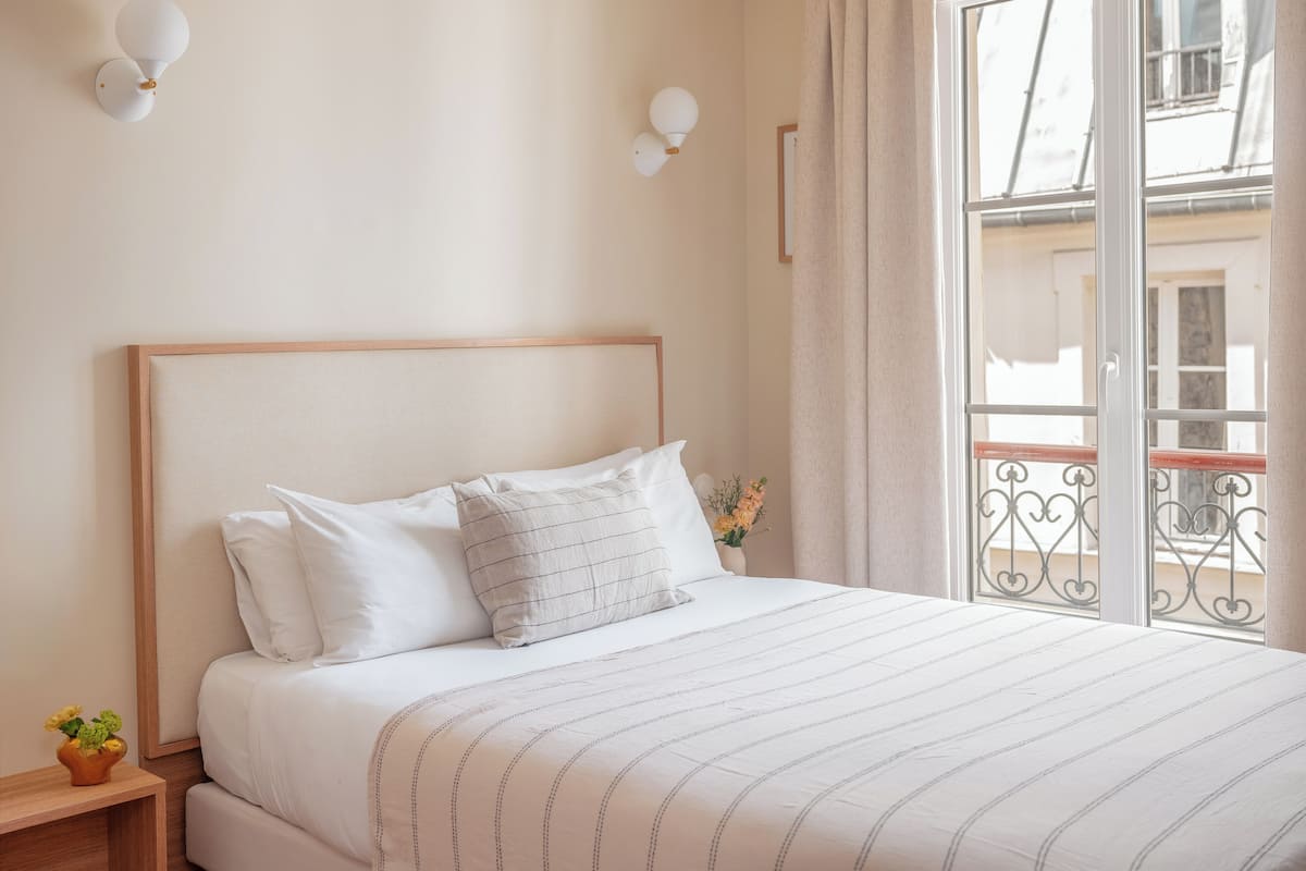 Un lit bien fait, avec une couvre-lit à rayures, une tête de lit en bois et deux appliques murales.
