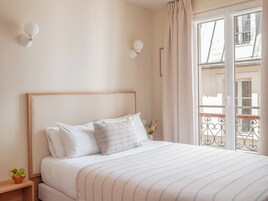 Un lit bien fait, avec une couvre-lit à rayures, une tête de lit en bois et deux appliques murales.