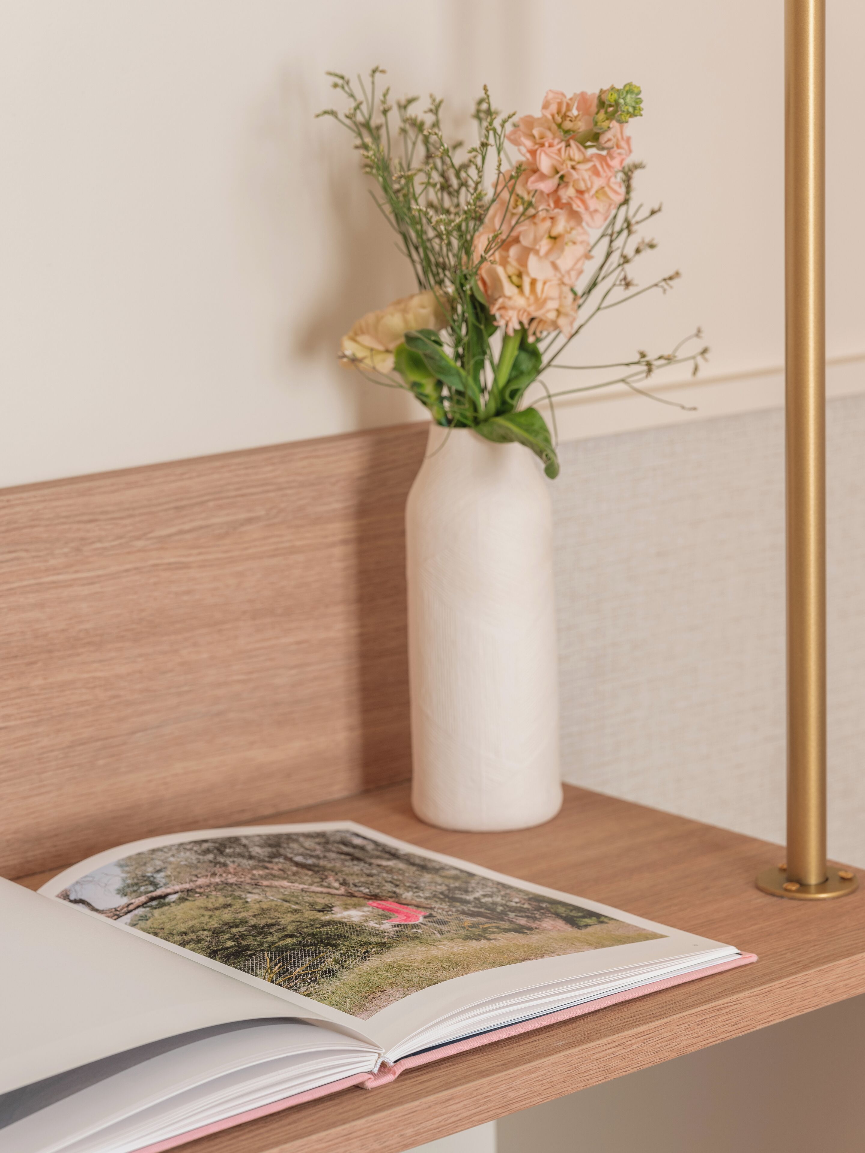 A book with a photograph on its pages, a white vase with flowers, and a wooden bench.