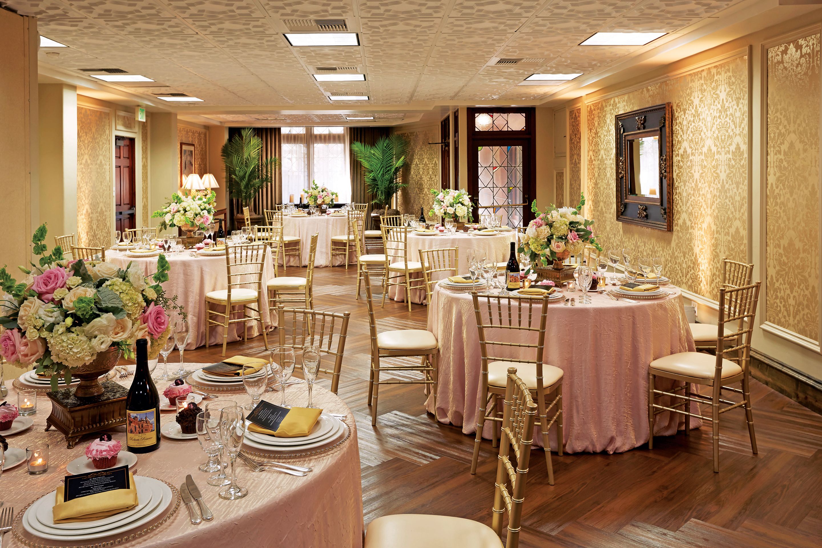 A banquet hall with round tables, gold chairs, and floral centerpieces.