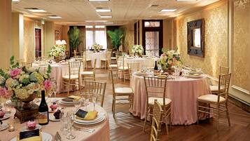 A banquet hall with round tables, gold chairs, and floral centerpieces.