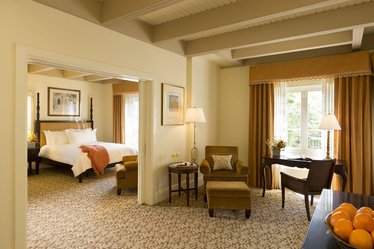 A hotel room with a bed, a desk, a chair, a small table, and a bowl of fruit.