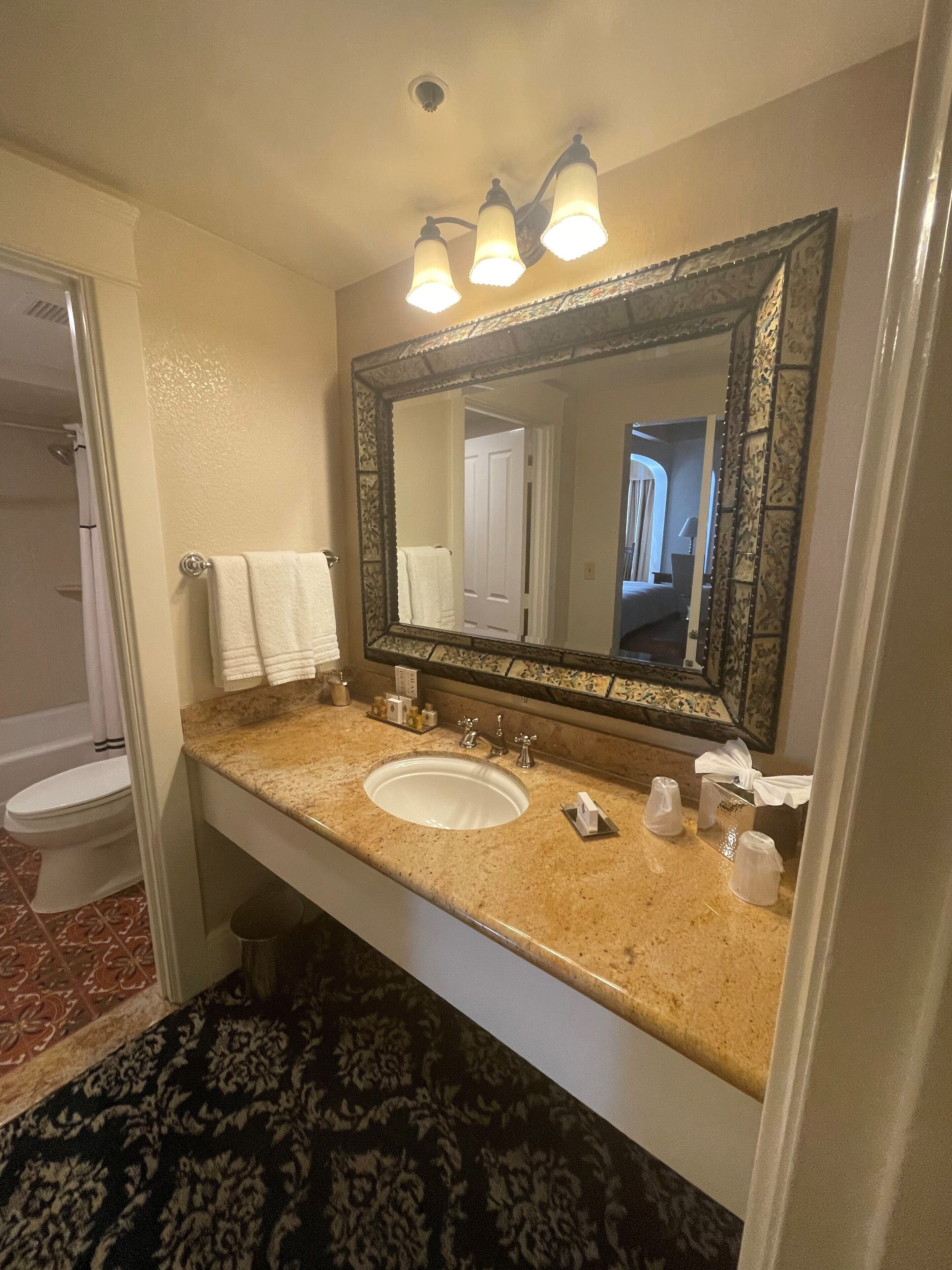 Un baño con lavamanos, espejo y perchero para toallas.
