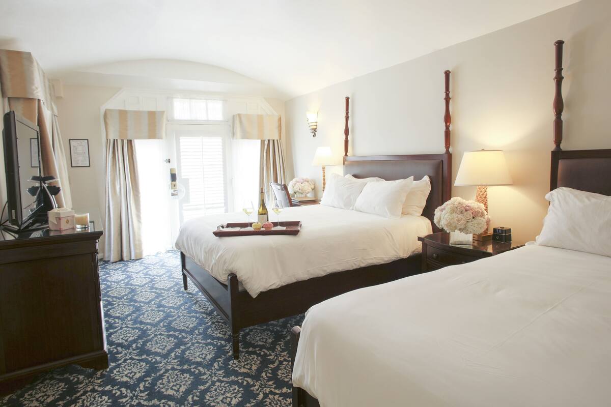 A hotel room with two beds, a dresser, and a large window with curtains.