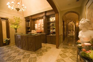 A lobby with a reception desk, a chandelier, a statue, and a patterned floor.