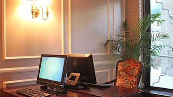 A hotel room with a desk, computer, chair, and a potted plant.