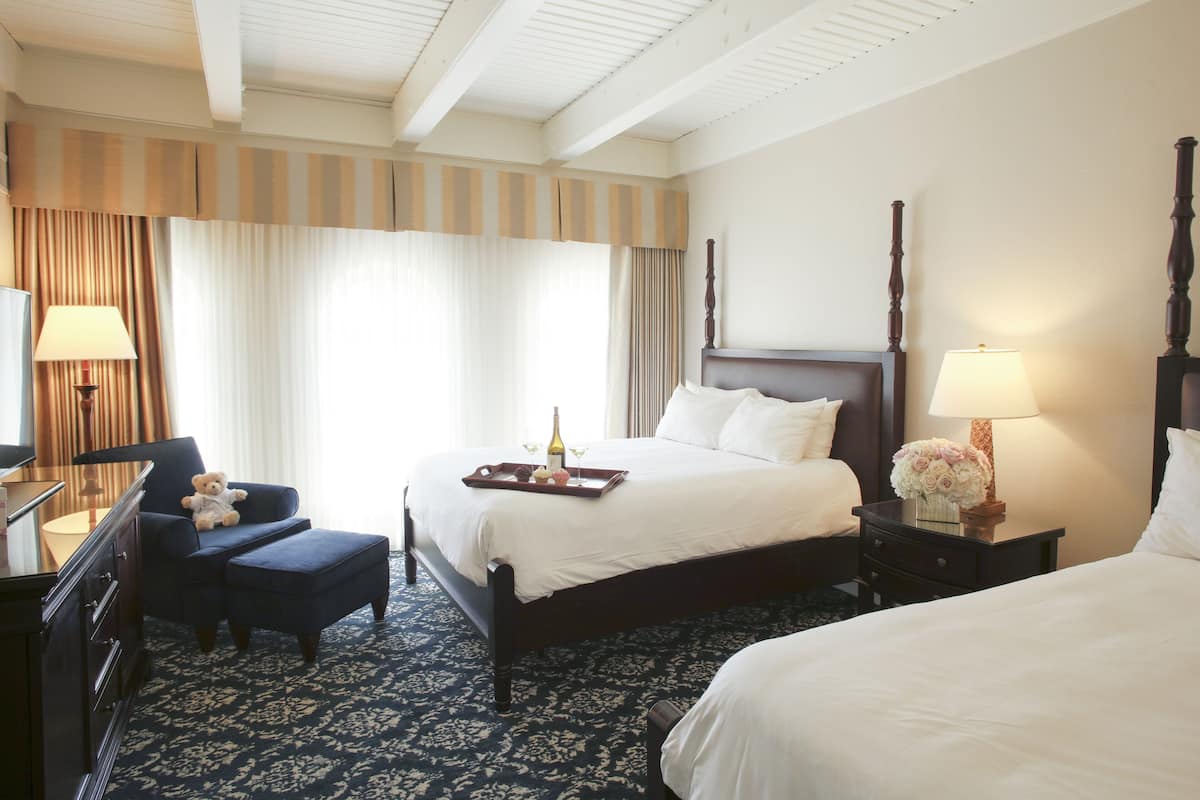 A hotel room with a large bed, a chair, a desk with a lamp, and a nightstand with a lamp.