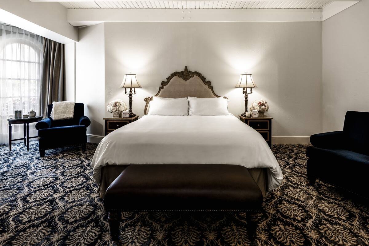 A neatly arranged hotel room with a large bed, two bedside tables with lamps, a chair, and a bench.