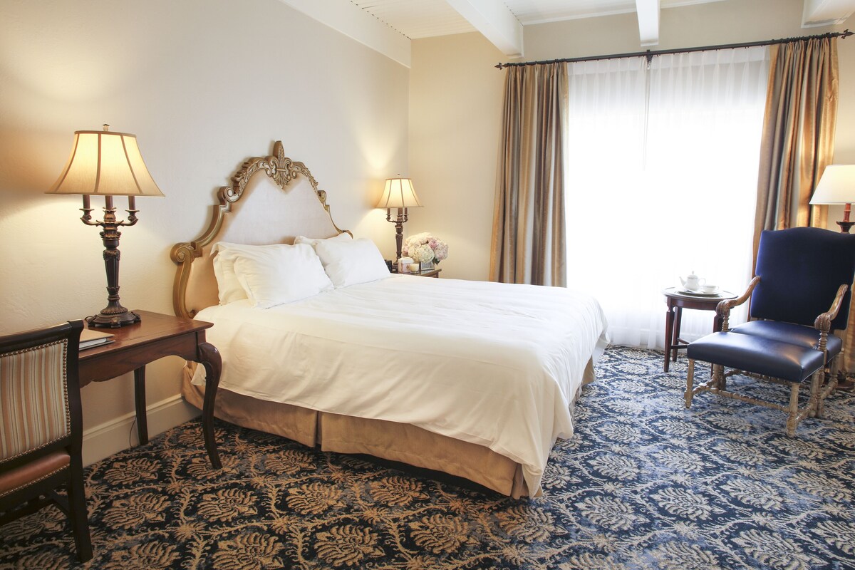 A hotel room with a large bed, two bedside tables with lamps, a chair, and a carpeted floor.