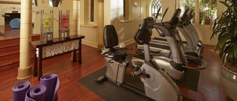 Ein Fitnessraum mit Trainingsgeräten, einer Bank und Yogamatten.
