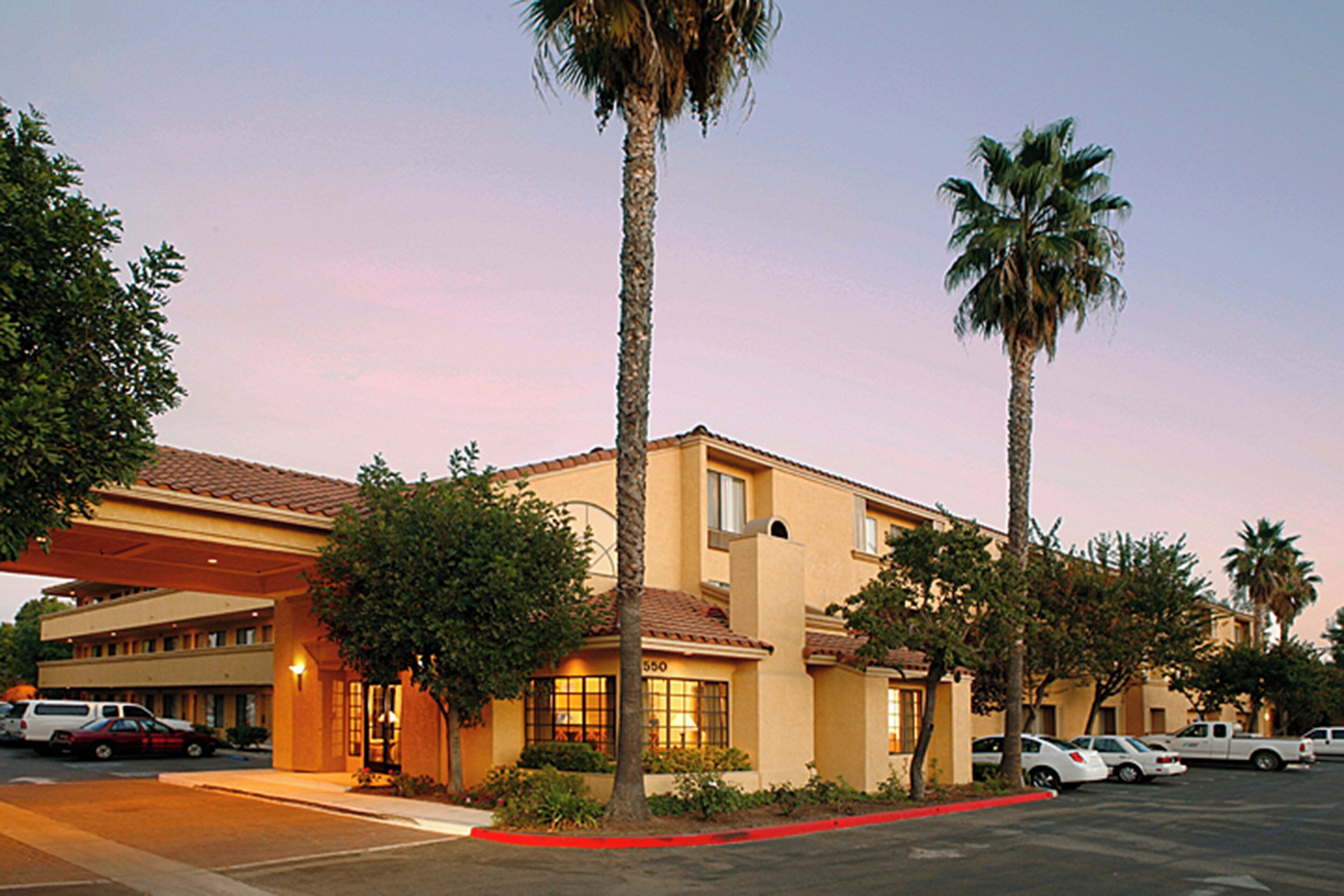 A hotel with a covered parking area, palm trees, and a building with a beige facade.