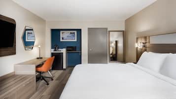 A hotel room with a bed, desk, chair, and a kitchenette area.