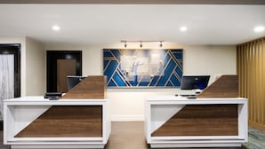 A reception desk with a modern design, featuring two white desks with wooden accents and a geometric wall art piece above.