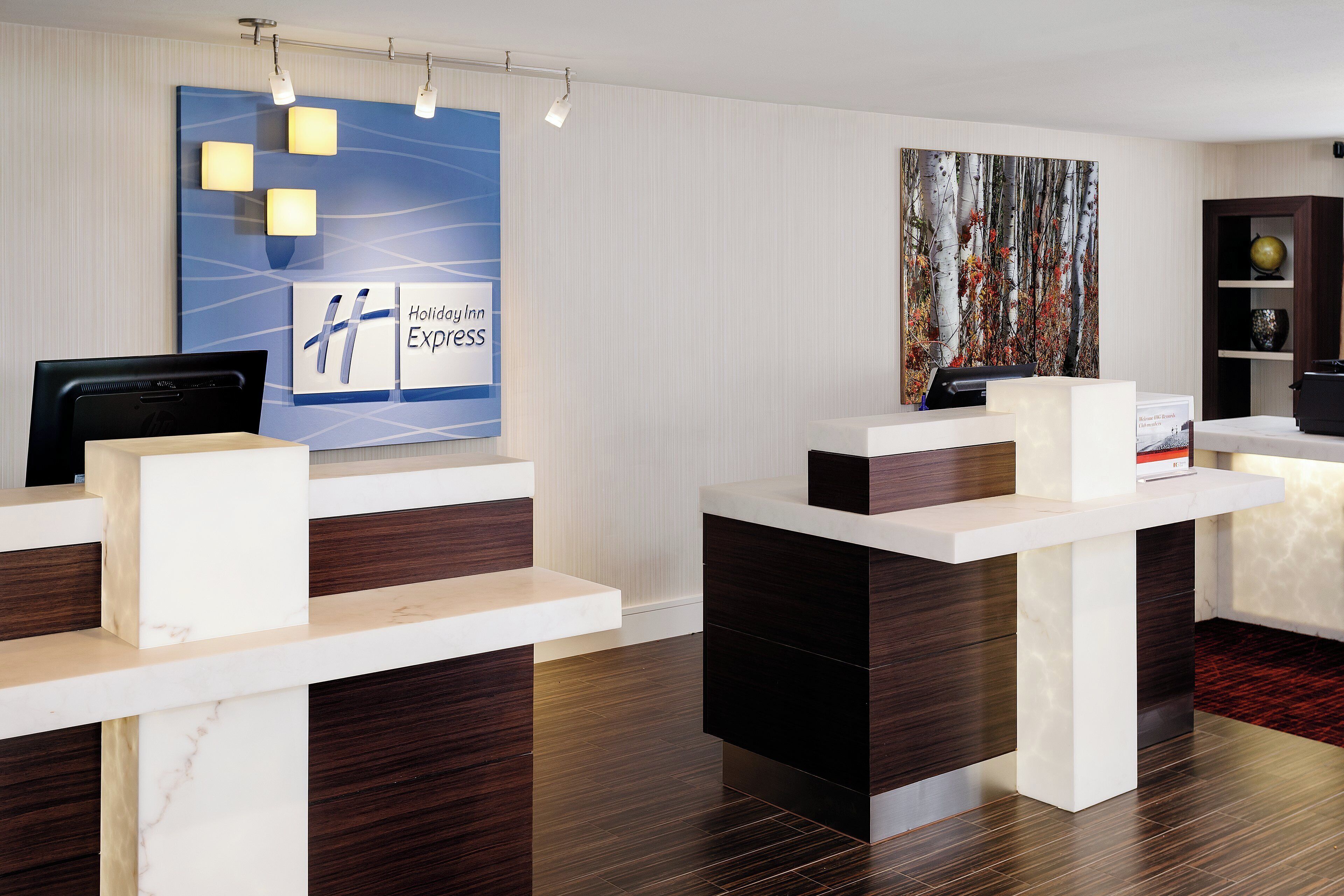 A hotel reception area with a modern design, featuring a reception desk, a digital screen, and a large wall art piece.