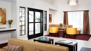 A modern hotel room with a sofa, two armchairs, a coffee table, and a large window with curtains.