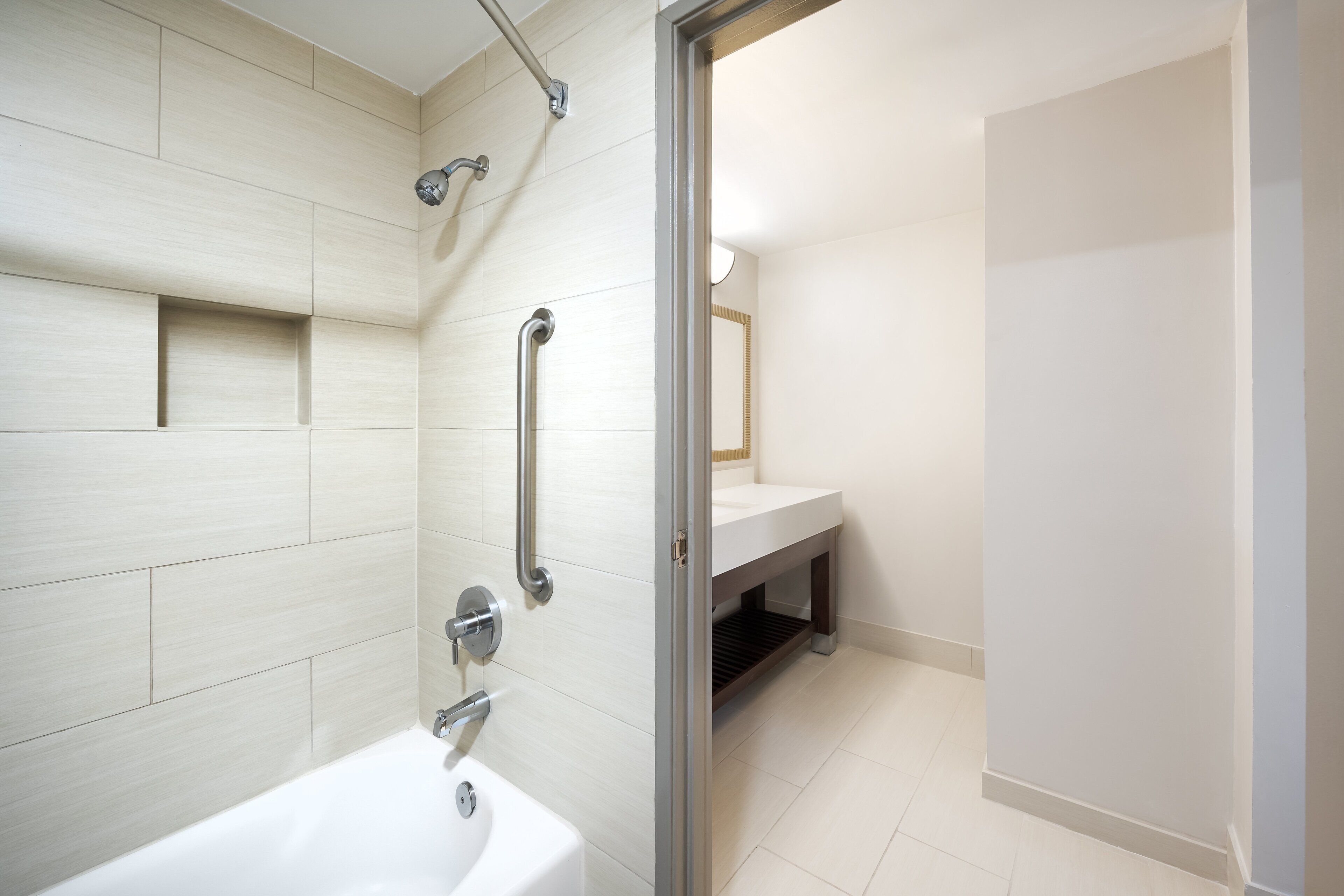 A modern bathroom with a bathtub, a shower with grab bars, and a vanity with a mirror.