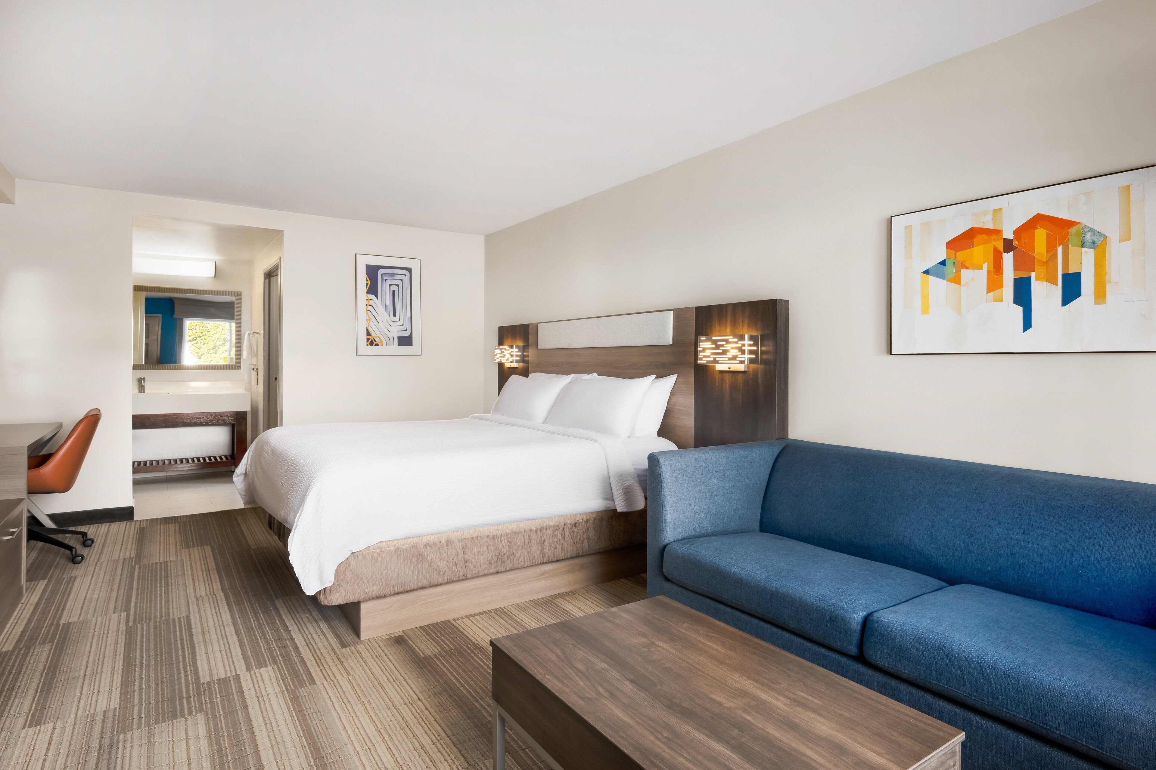 A hotel room with a bed, a blue sofa, a desk, and a chair.
