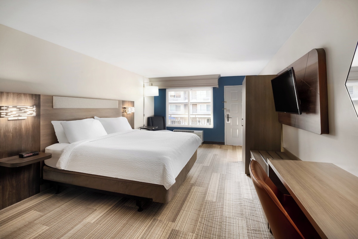 Une chambre d’hôtel moderne dotée d’un grand lit, d’un bureau, d’une télévision à écran plat et d’une fenêtre donnant sur des immeubles.