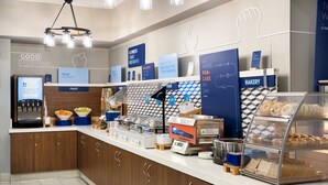 A modern breakfast bar with a digital coffee machine, a fruit display, and a bakery section.