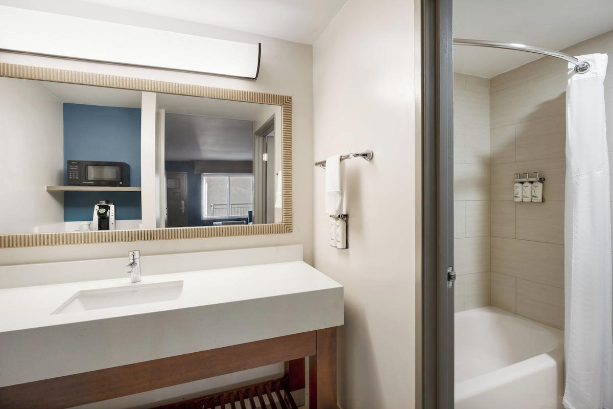 Une salle de bain avec un lavabo blanc, un miroir, un rideau de douche et une baignoire.