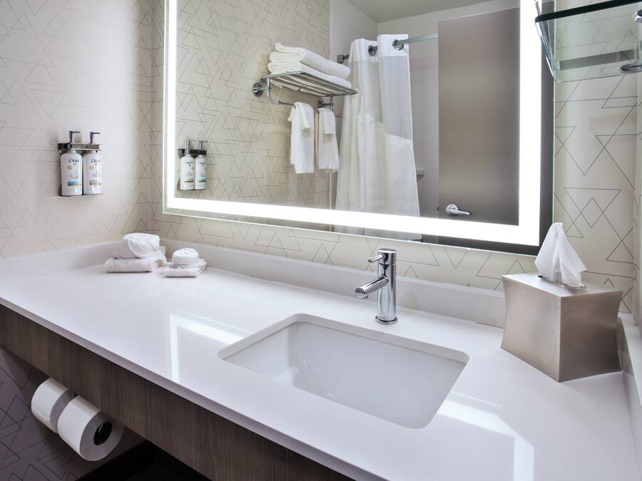 Un baño moderno con un espejo grande, lavamanos blanco y toallas ordenadas.