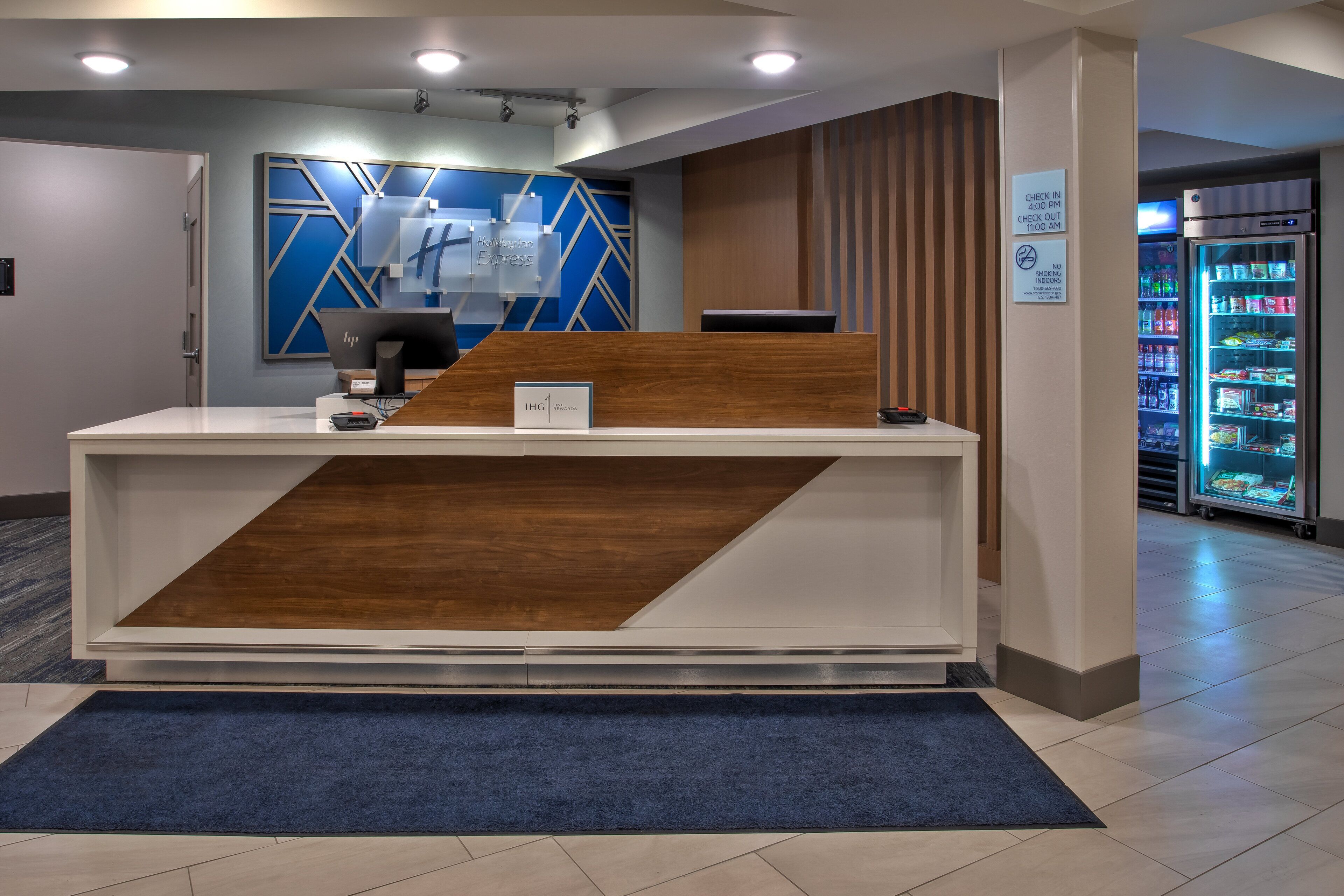 A reception desk with a blue and white color scheme, a digital screen, and a sign indicating check-in times.