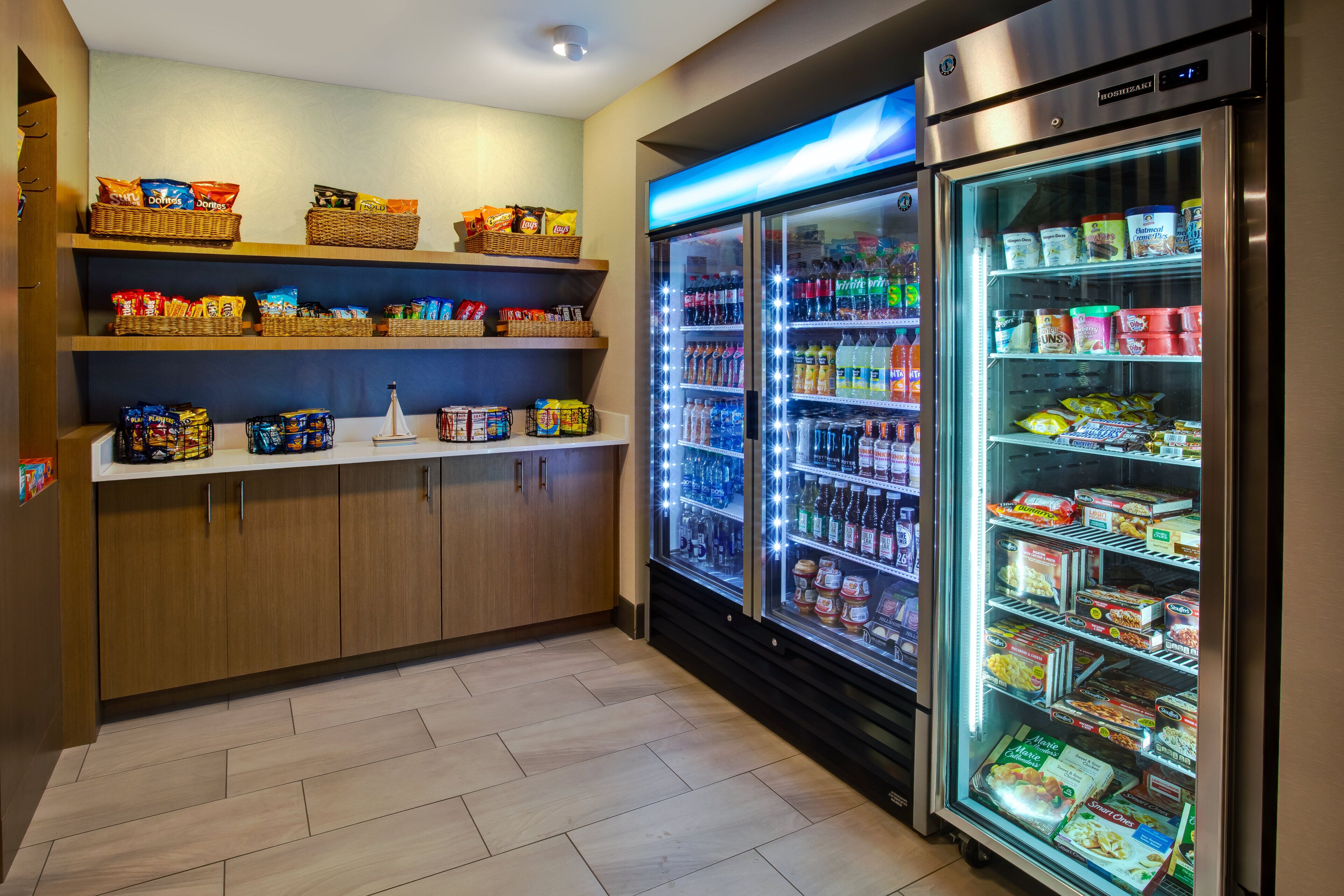 A kitchenette with shelves stocked with snacks, a refrigerator with beverages, and a microwave.