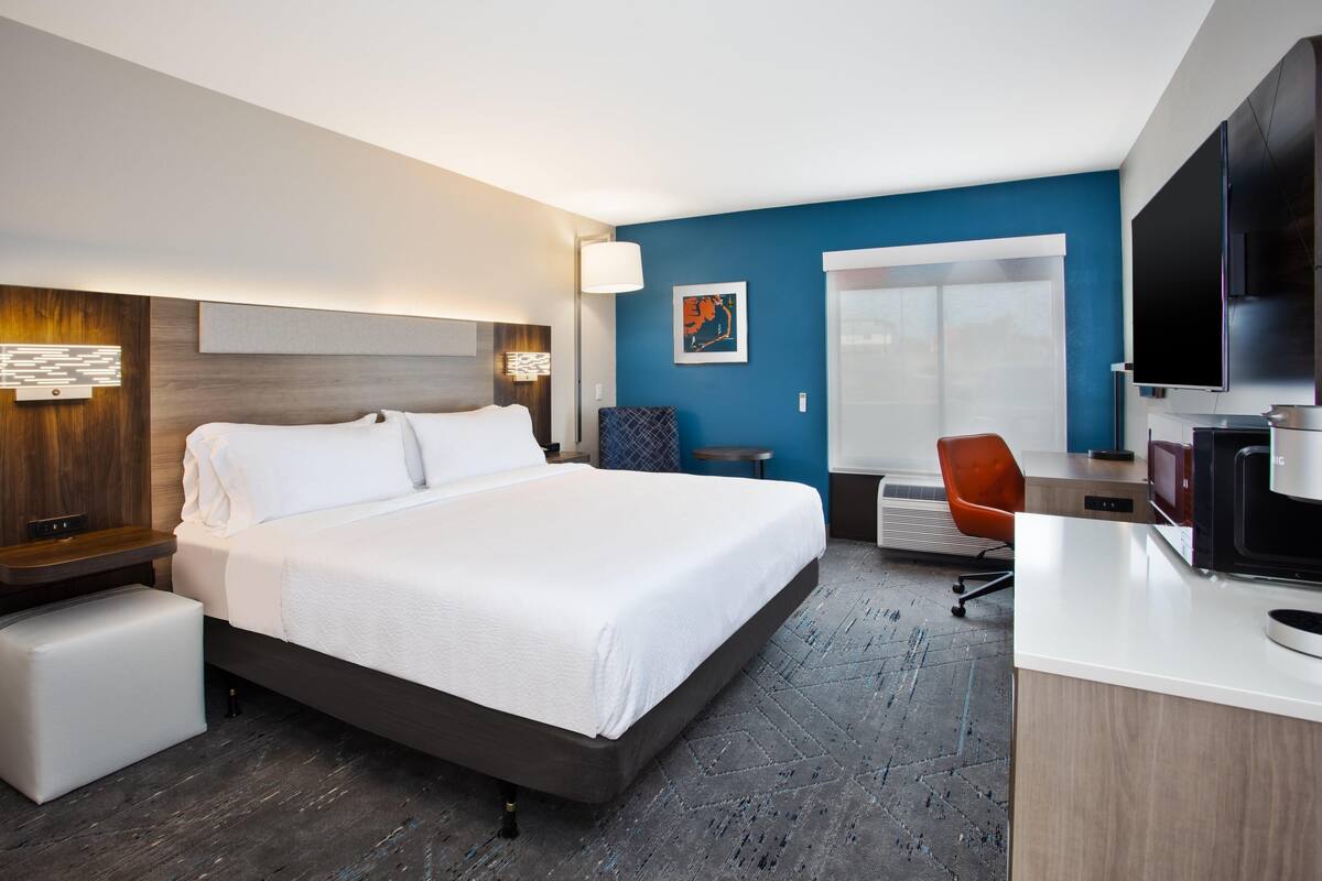 A hotel room with a large bed, a desk with a computer, a chair, and a television.