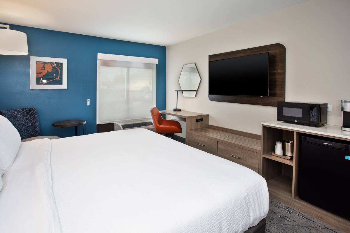 A hotel room with a large bed, a desk with a computer, a TV, and a microwave.