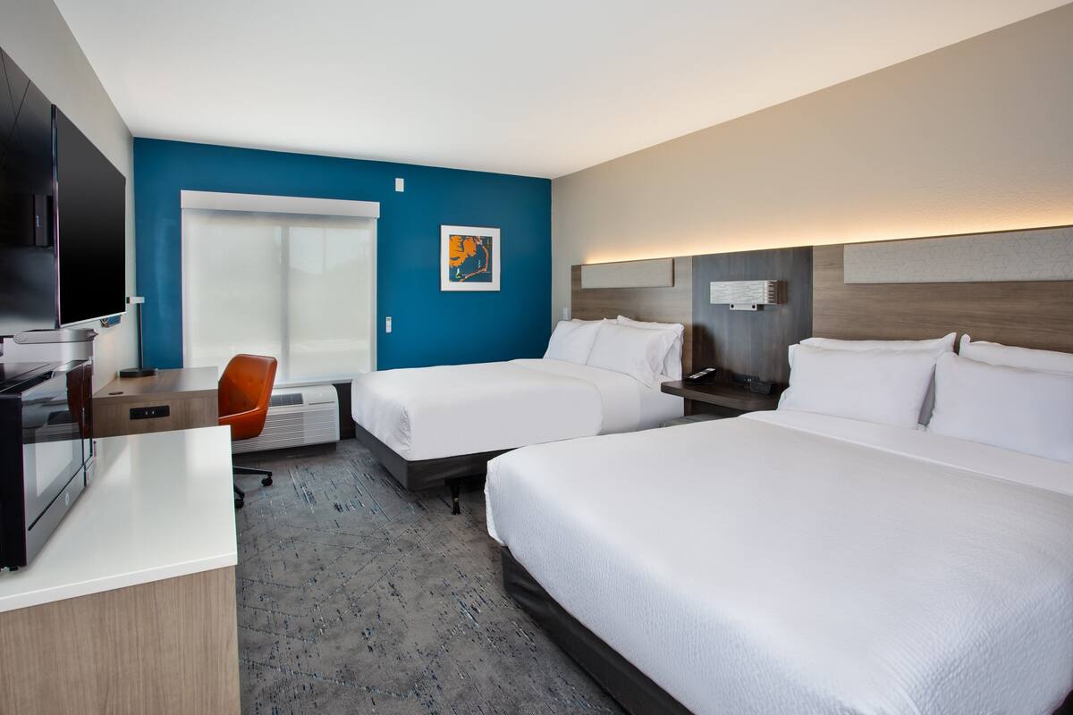 A hotel room with two beds, a desk, a chair, a TV, and a window.
