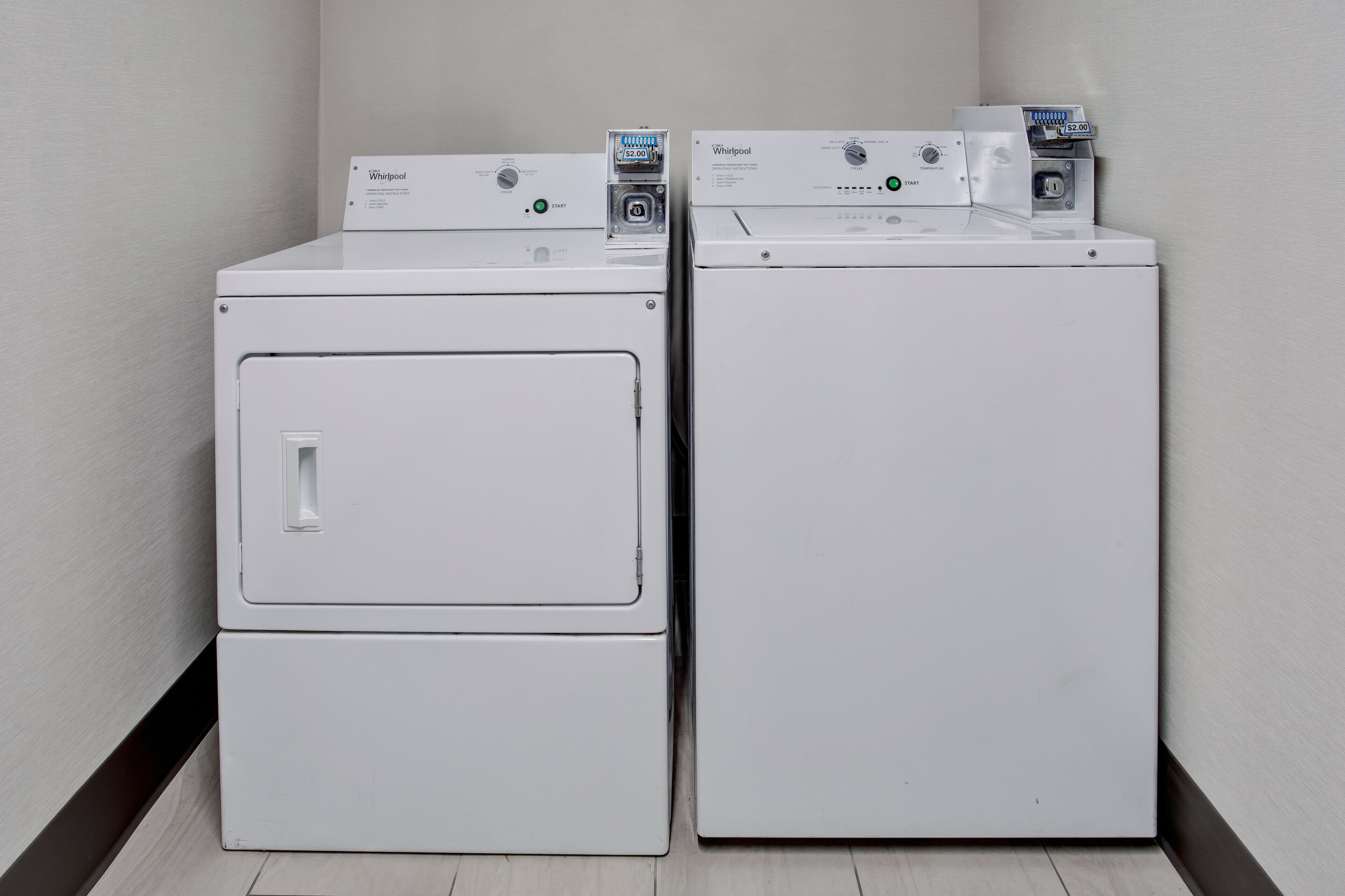 Two stacked front-loading washers in a corner with a wooden floor and plain walls.