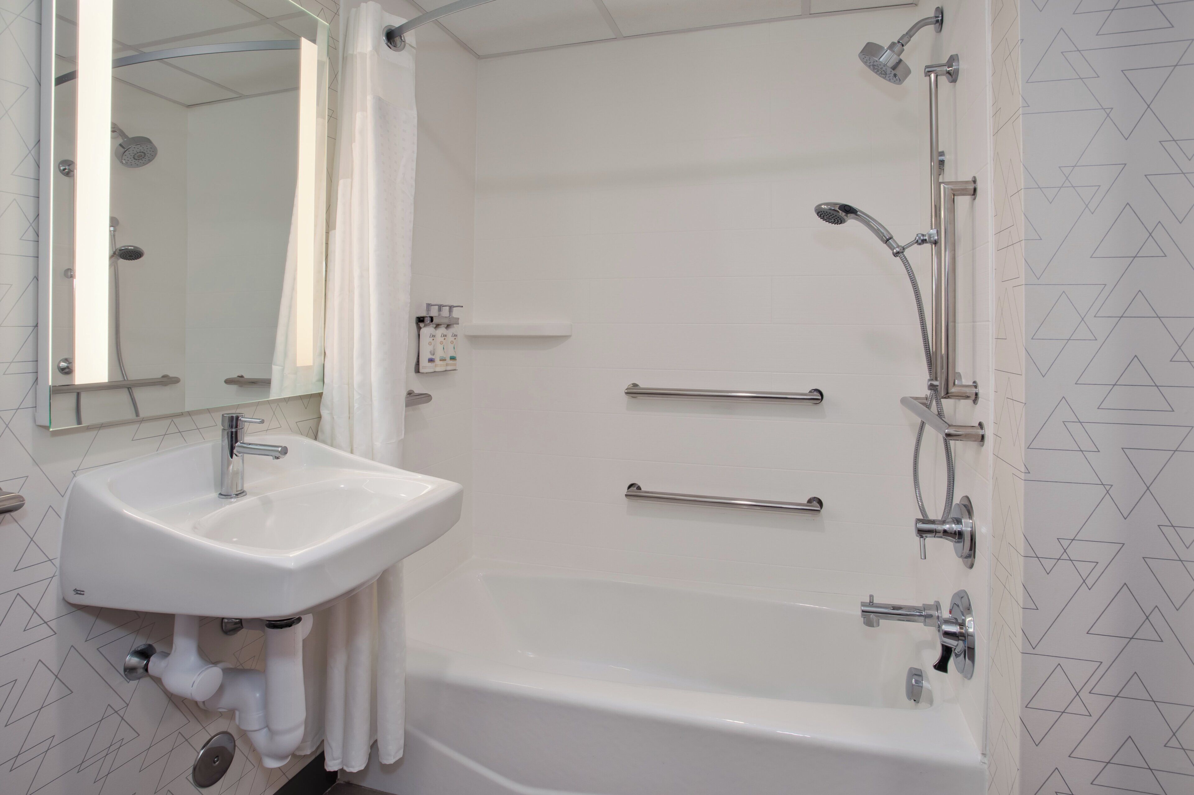 A bathroom with a white sink, a bathtub, a shower with a handheld showerhead, and a mirror.