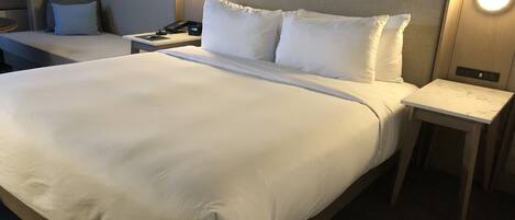 A hotel room with a large bed, two bedside tables, a nightstand, and a wall-mounted light fixture.