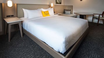 Ett hotellrum med en stor säng, två sängbord, ett litet skrivbord, en stol och ett runt bord.