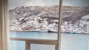 Una habitación con un gran ventanal que ofrece vistas a un paisaje nevado y un cuerpo de agua. Una mesa redonda con un cuenco decorativo está ubicada frente a la ventana.