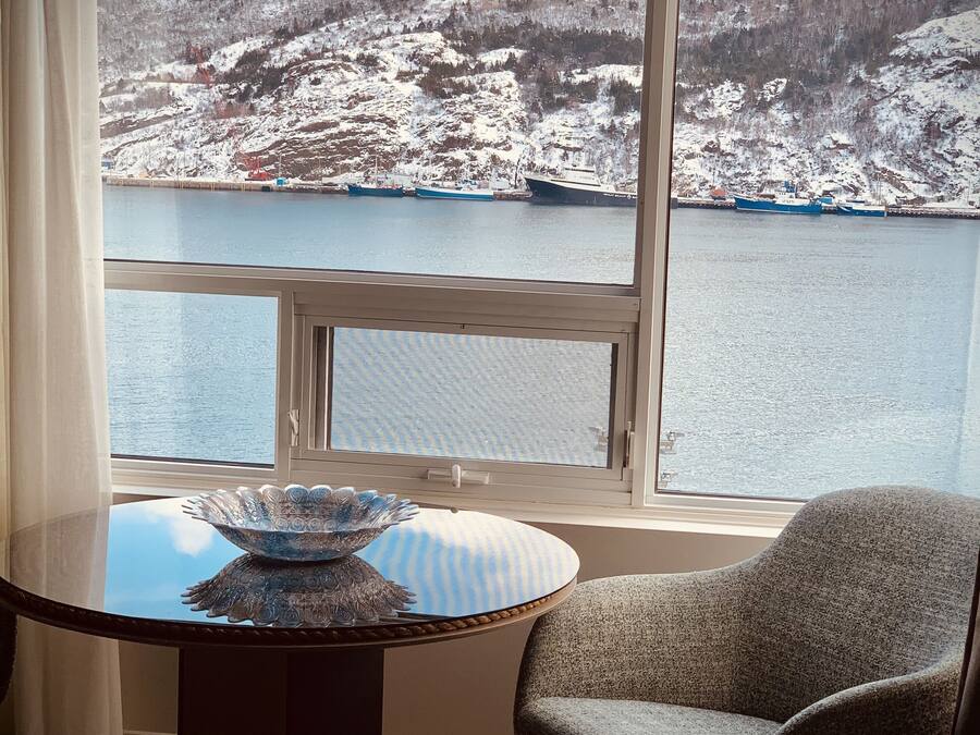 Una habitación con un gran ventanal que ofrece vistas a un paisaje nevado y un cuerpo de agua. Una mesa redonda con un cuenco decorativo está ubicada frente a la ventana.