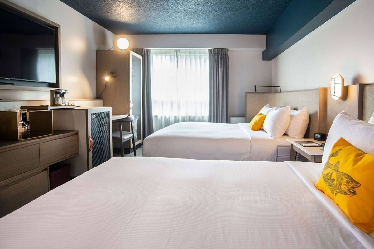 A hotel room with two beds, a desk, a television, and a window with curtains.