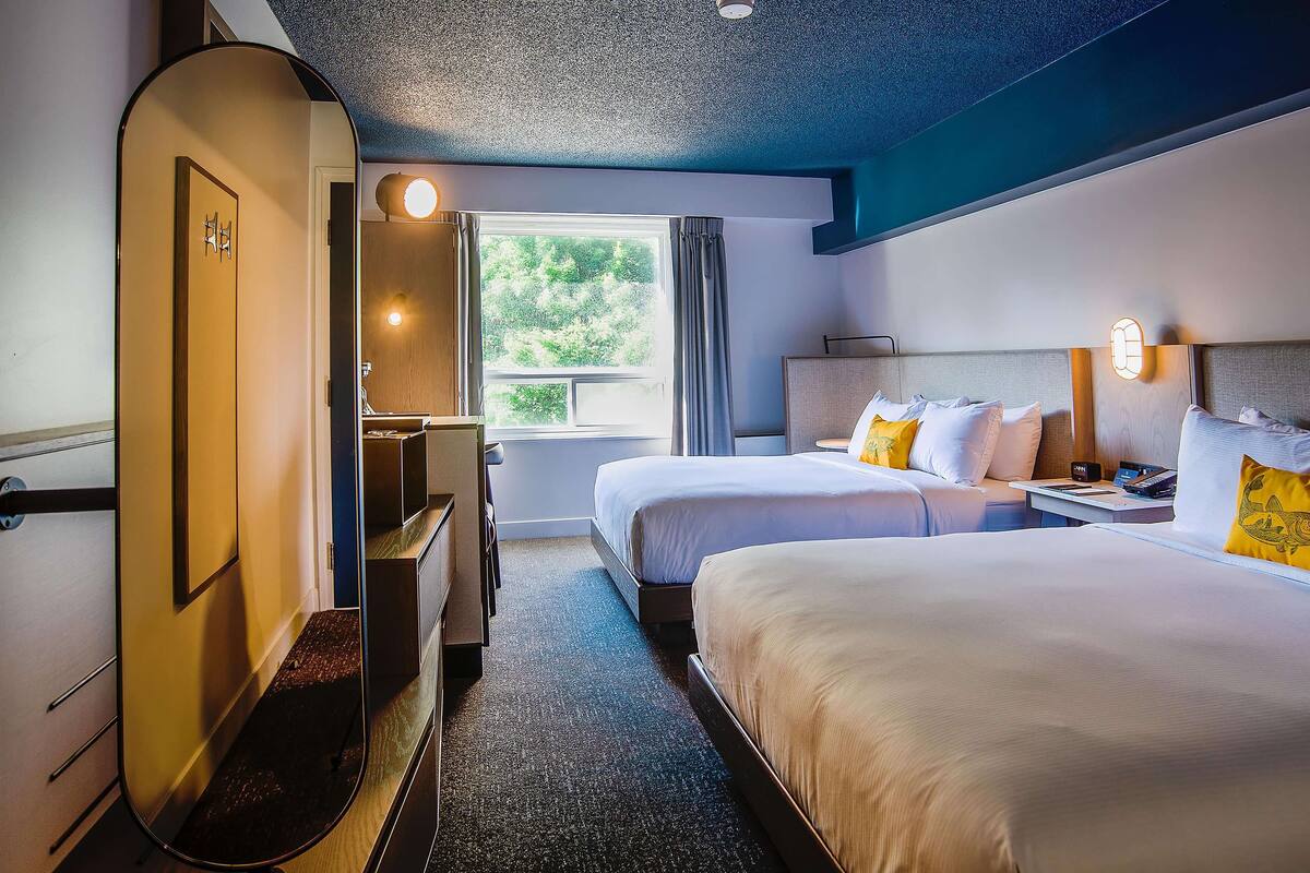 A hotel room with two beds, a desk, a chair, and a window with curtains.