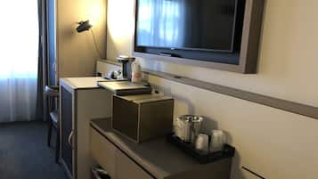Una camera d'albergo con una scrivania, una televisione a muro, una macchina per il caffè e un cestino.