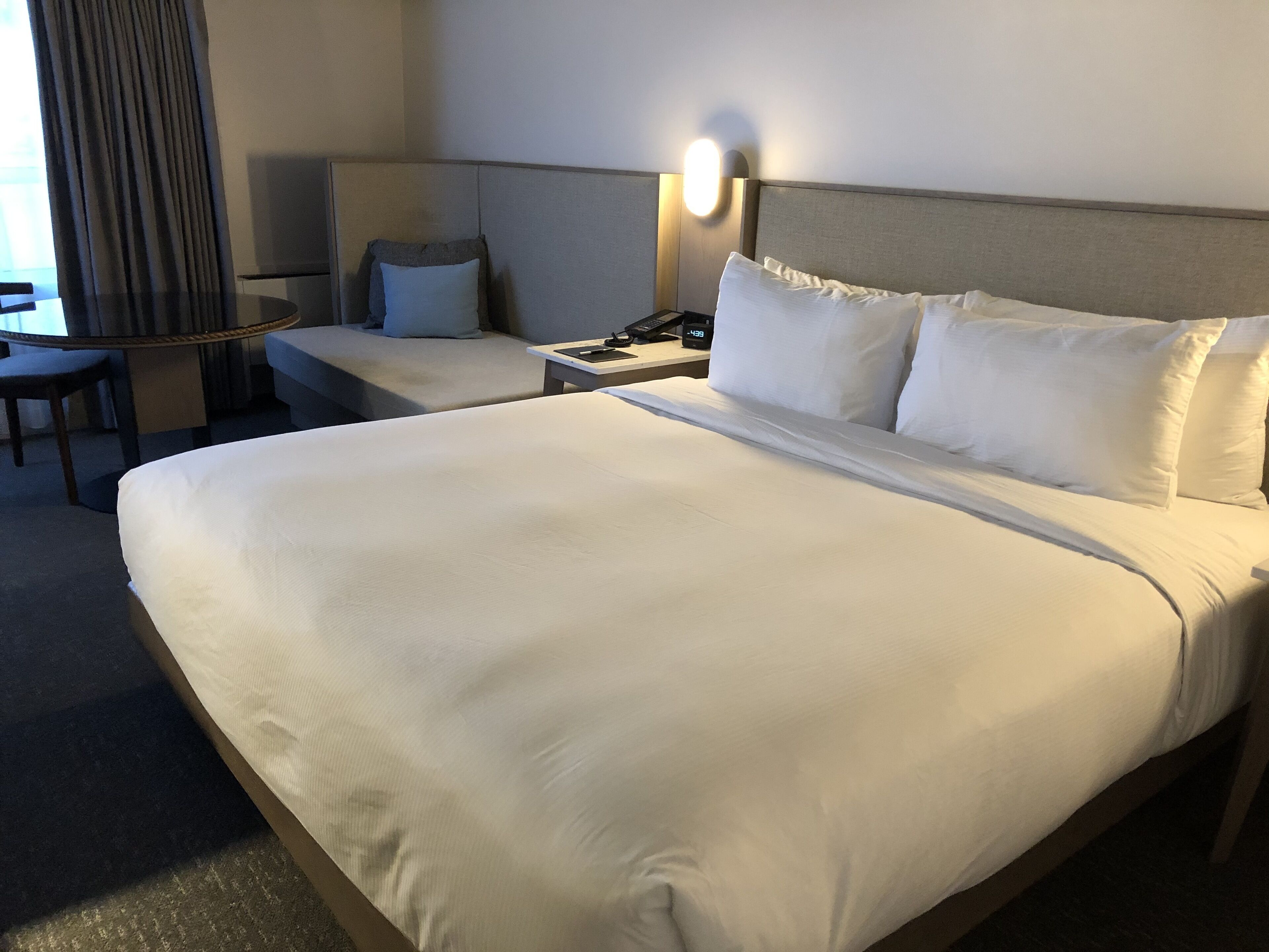 Een hotelkamer met een groot bed, een nachtkastje met een lamp, een stoel en een bureau met een computer.