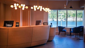 Zona de recepción de hotel con un mostrador de madera, vista a una masa de agua a través de amplios ventanales e iluminación moderna.