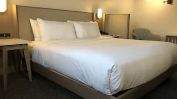 Una cama bien hecha con sábanas blancas, una mesita de noche con una lámpara y una silla en una habitación de hotel moderna.
