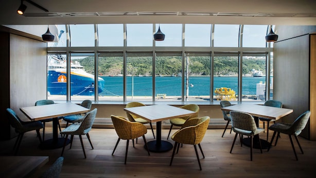 Comedor con amplios ventanales que dan a un puerto, mostrando un barco y construcciones industriales.